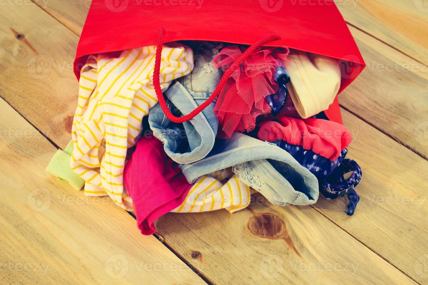 Women's clothing falls out of paper shopping bags on wooden background. photo