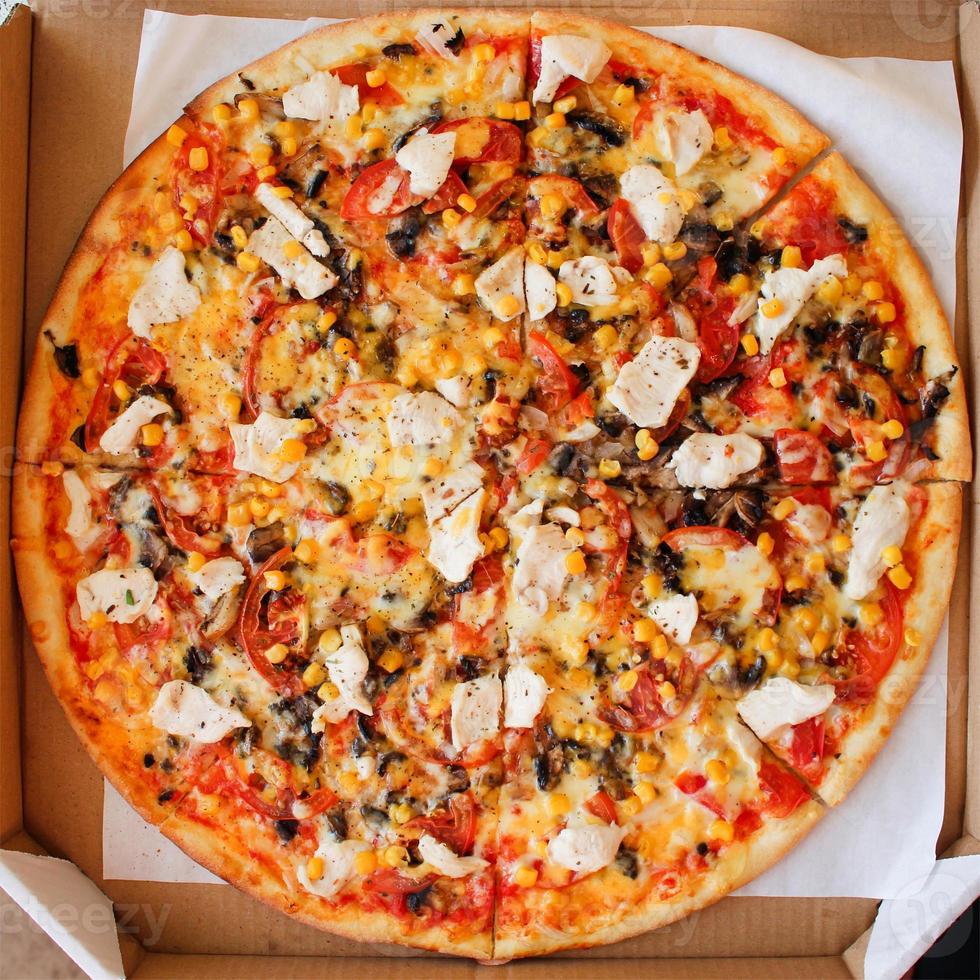 Closeup of pizza with chicken, tomatoes, corn, cheese, mushrooms and spices. Top view. photo