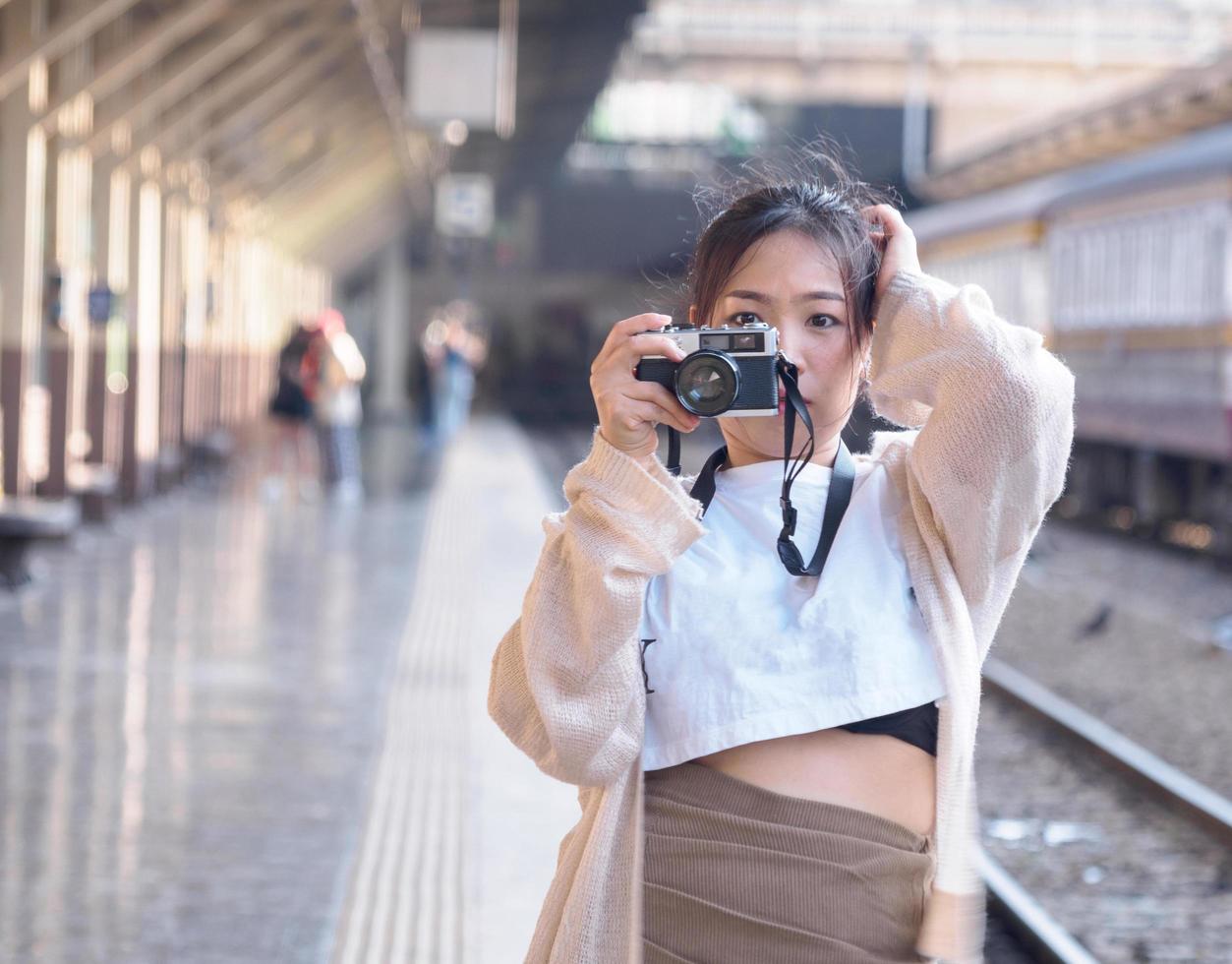 retrato fotografía yong niña asiático mujer hermosa frio largo pelo vistiendo blanco camisa modelo con retro película cámara en pie a tren estación bangkok, viaje en vacaciones durante noche de el día. foto