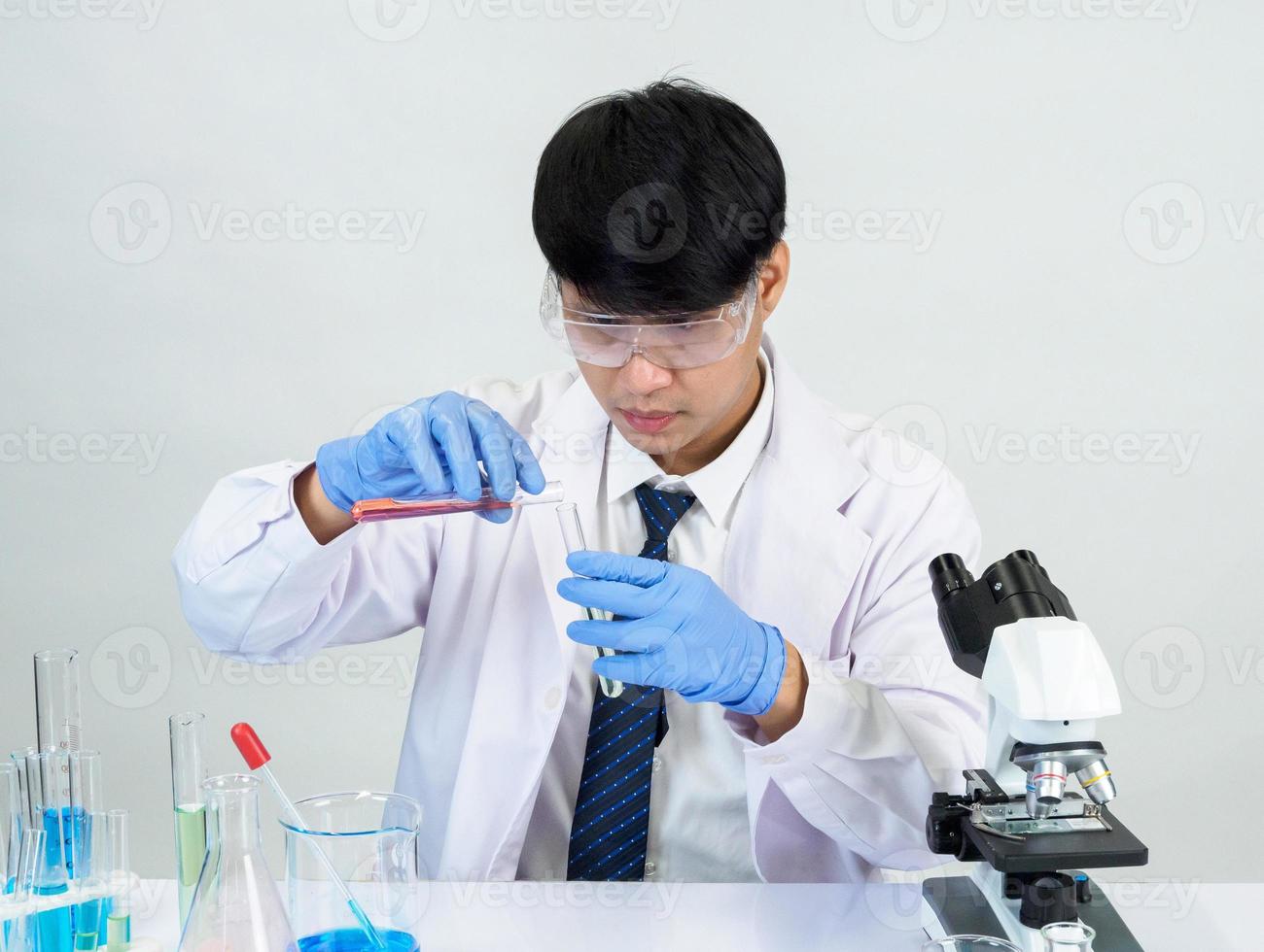 estudiante científico asiático en un laboratorio de mezcla de reactivos en un laboratorio de investigación científica con tubos de ensayo de varios tamaños y microscopios. sobre la mesa en el fondo blanco de laboratorio de química de laboratorio. foto