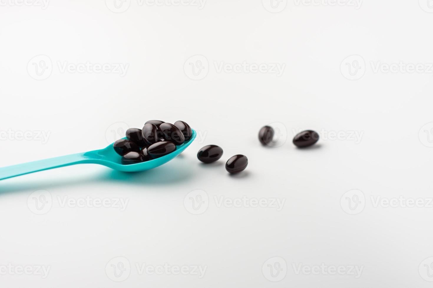 Black soft gel capsules in a blue spoon on a white background. Vitamin food supplements photo