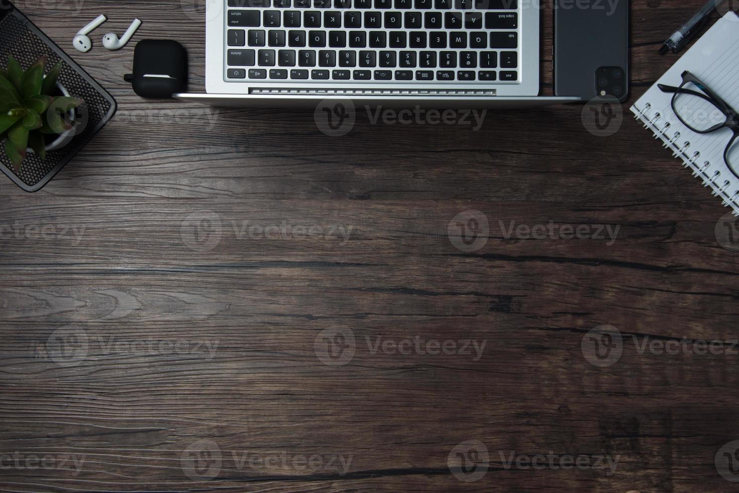 wooden office desk with laptop, blank notebook, cordless earphones and glasses, dark background, wooden background, Top view with copy space, empty space. photo