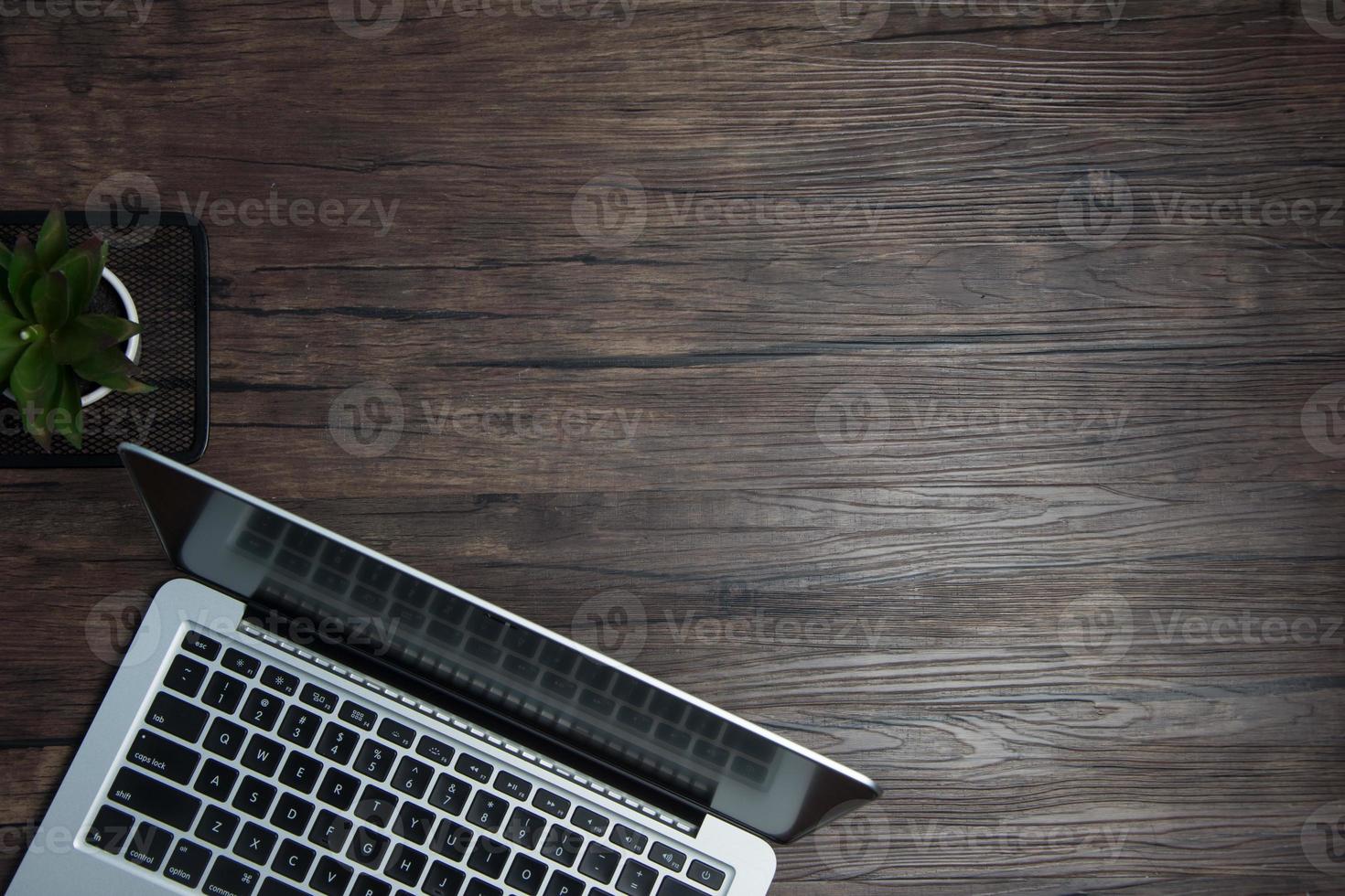 wooden office desk with laptop, blank notebook, cordless earphones and glasses, dark background, wooden background, Top view with copy space, empty space. photo