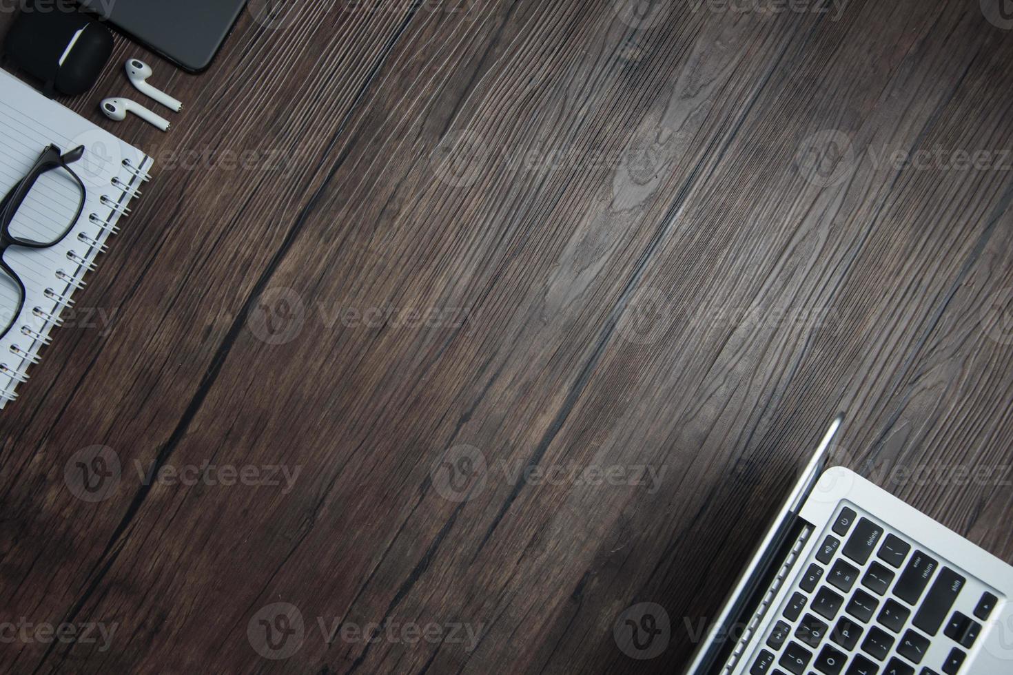 de madera oficina escritorio con computadora portátil, blanco computadora portátil, sin cable auriculares y anteojos, oscuro fondo, de madera fondo, parte superior ver con Copiar espacio, vacío espacio. foto