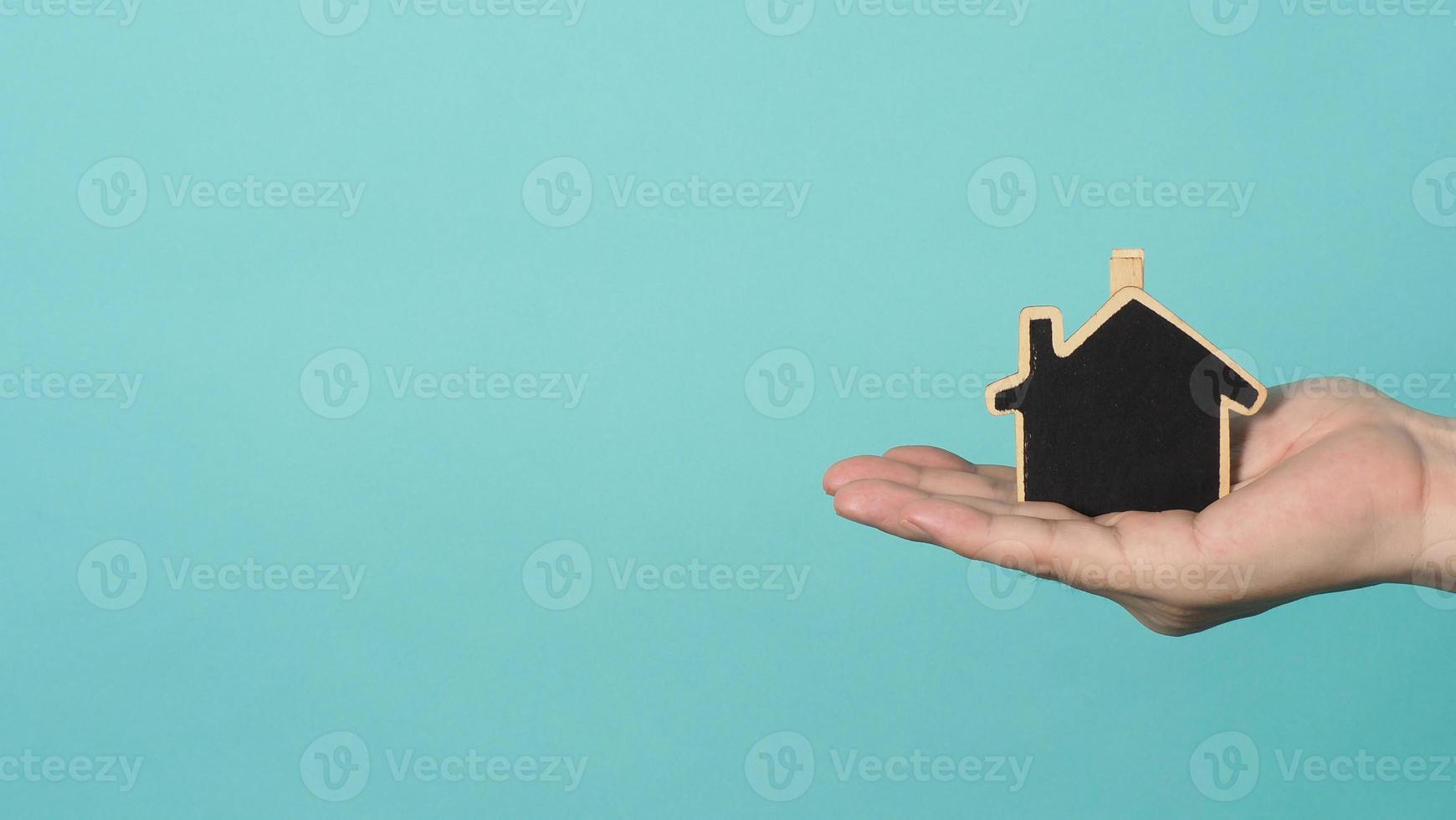 Small wood house in hands represent concepts such as home care family love real estate housing shelter insurance and mortgage. Hands holding small model house isolated on blue green studio background. photo
