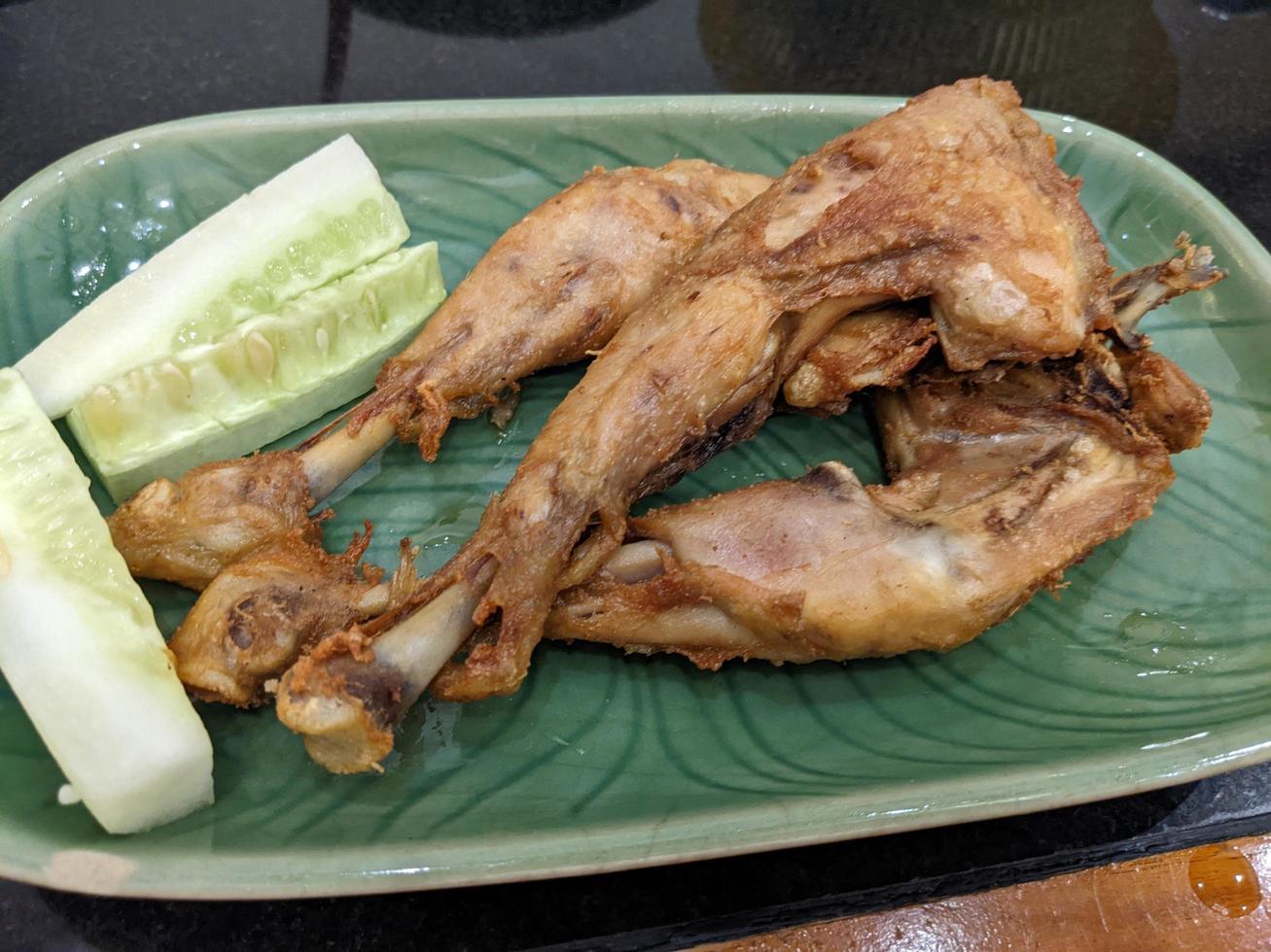 Fried Chicken with cucumber slice with green plate on the Indonesia traditional restaurant. The photo is suitable to use for food background, poster and food content.