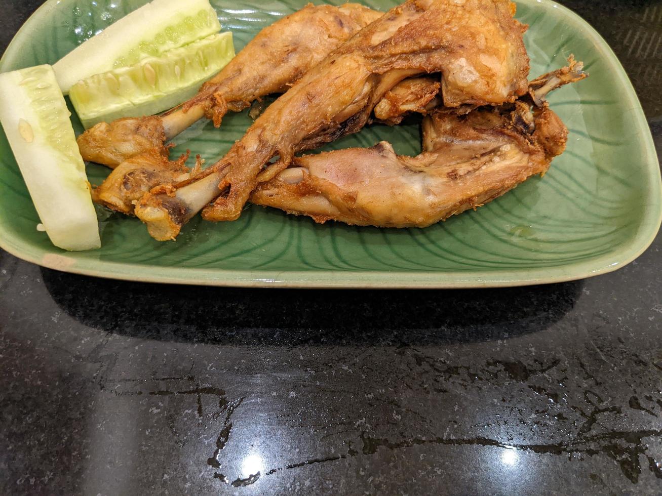Fried Chicken with cucumber slice with green plate on the Indonesia traditional restaurant. The photo is suitable to use for food background, poster and food content.