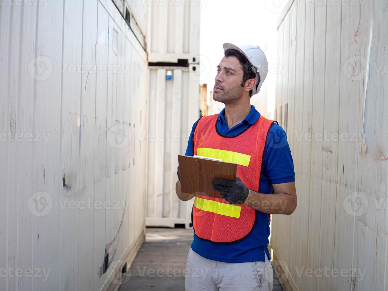 Male person stand walk recheck checklist report paper tablet technology import export cargo warehouse terminal storage white hat helmet safety freight work job occupation container loading dock shelf photo
