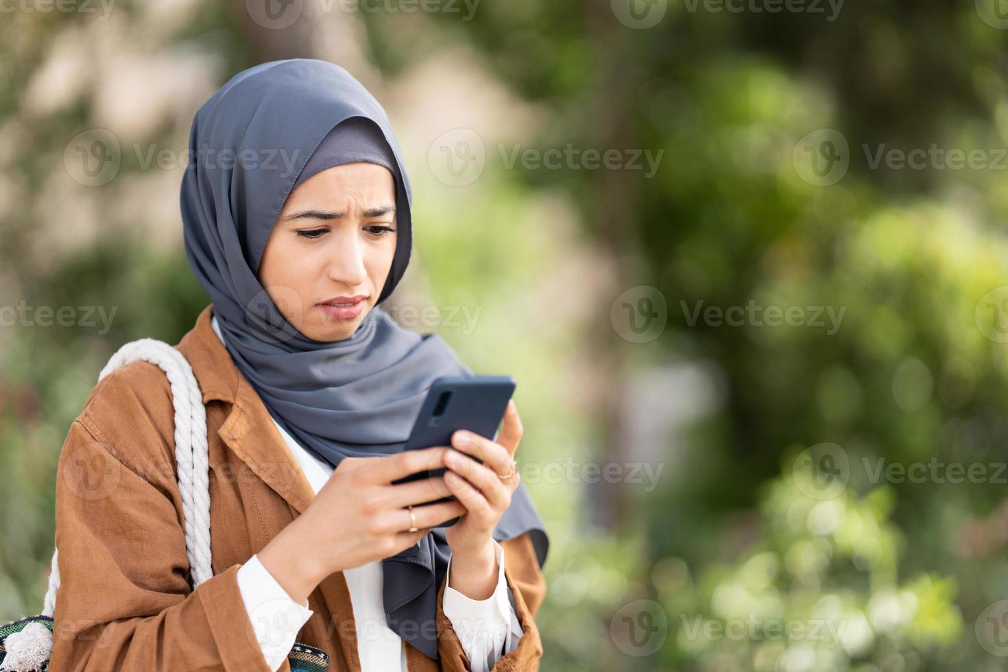 Muslim woman using mobile with a sad expression of disgust photo