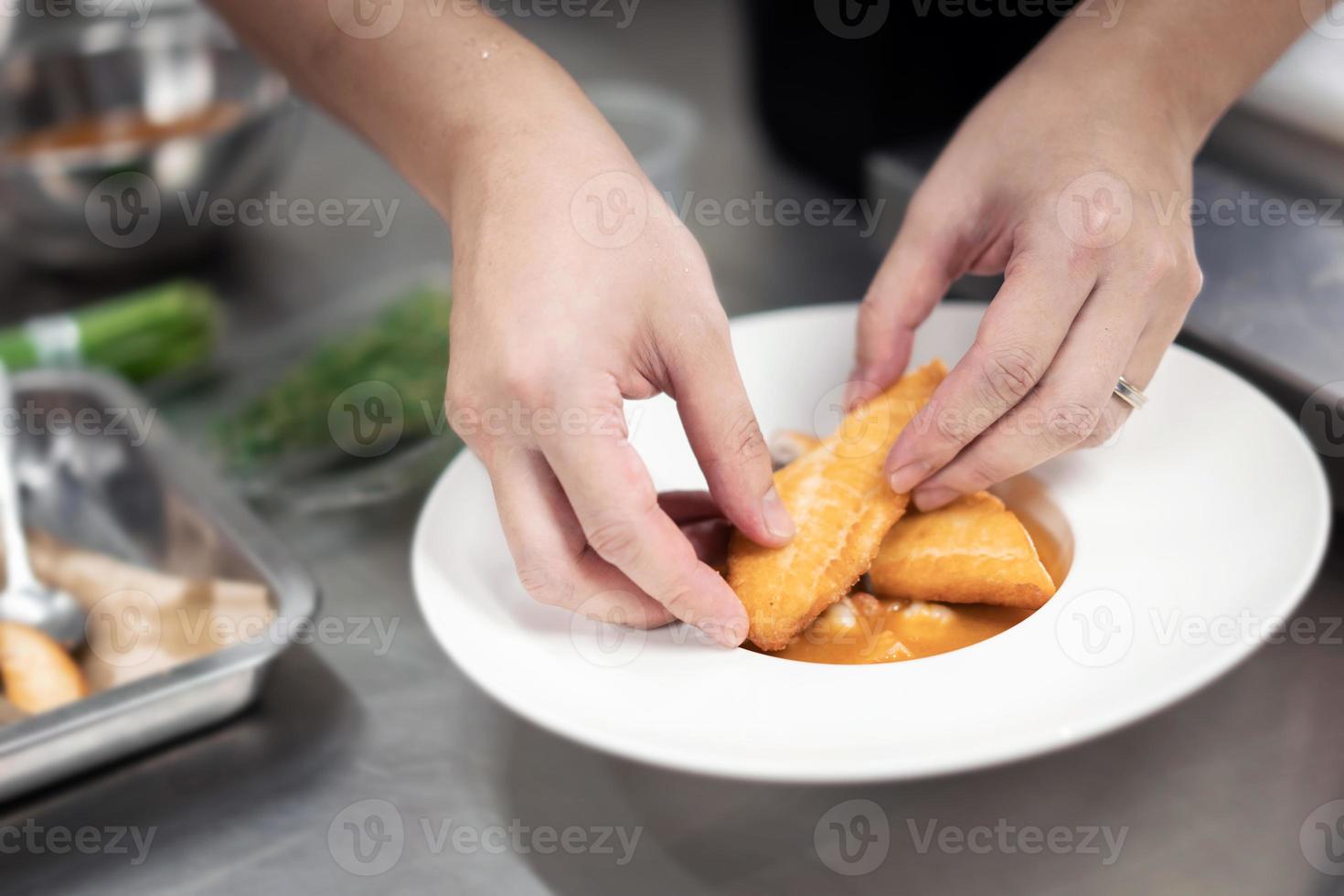 Focused hand male chef in  uniform decorate food, garnishes, prepare dish , in white plate in kitchen. photo