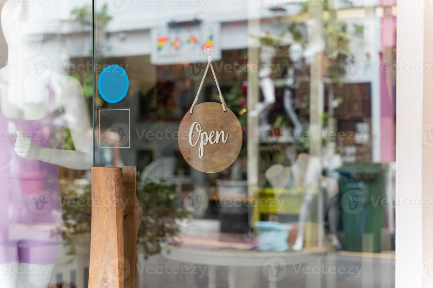 A business sign that says Open on local businesses hang on door at entrance. Say Welcome. Open and closed flip sign in front of shop glass door. photo