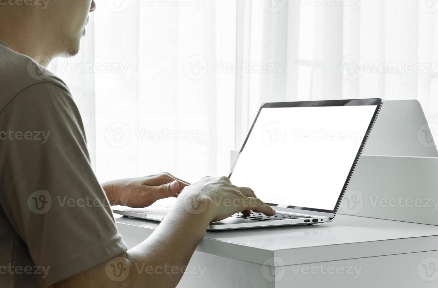 Man's hands using laptop with blank screen on white table at home or office. photo