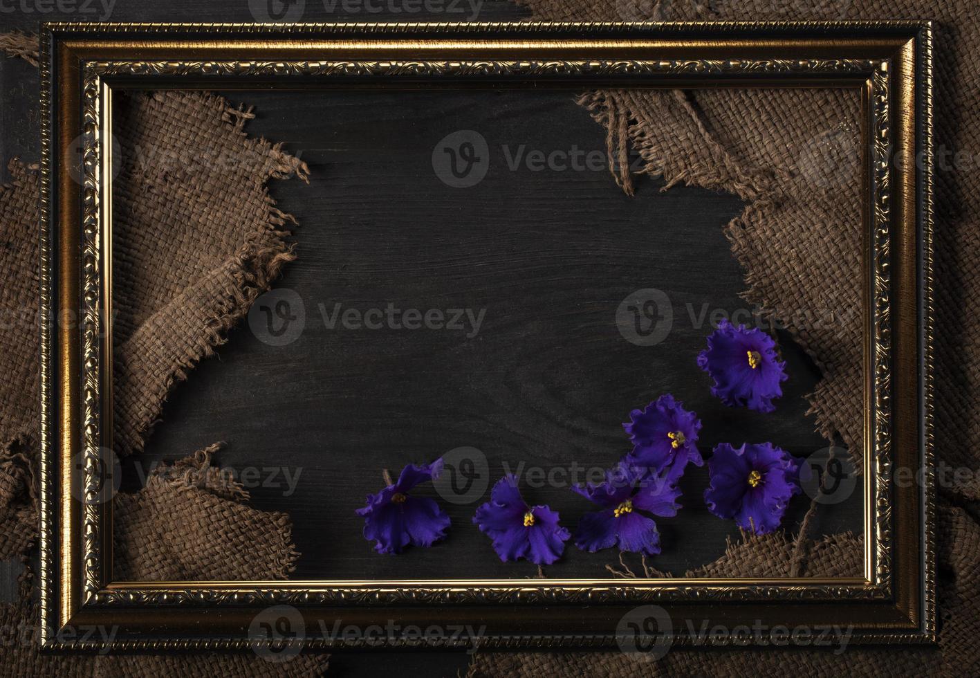 In a beautiful frame, a coarse weave fabric on a wooden background. and violet flowers. Background for the inscription. photo