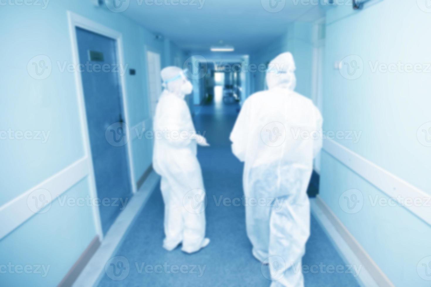 Blurred background of hospital corridor with doctors in protective suits. photo