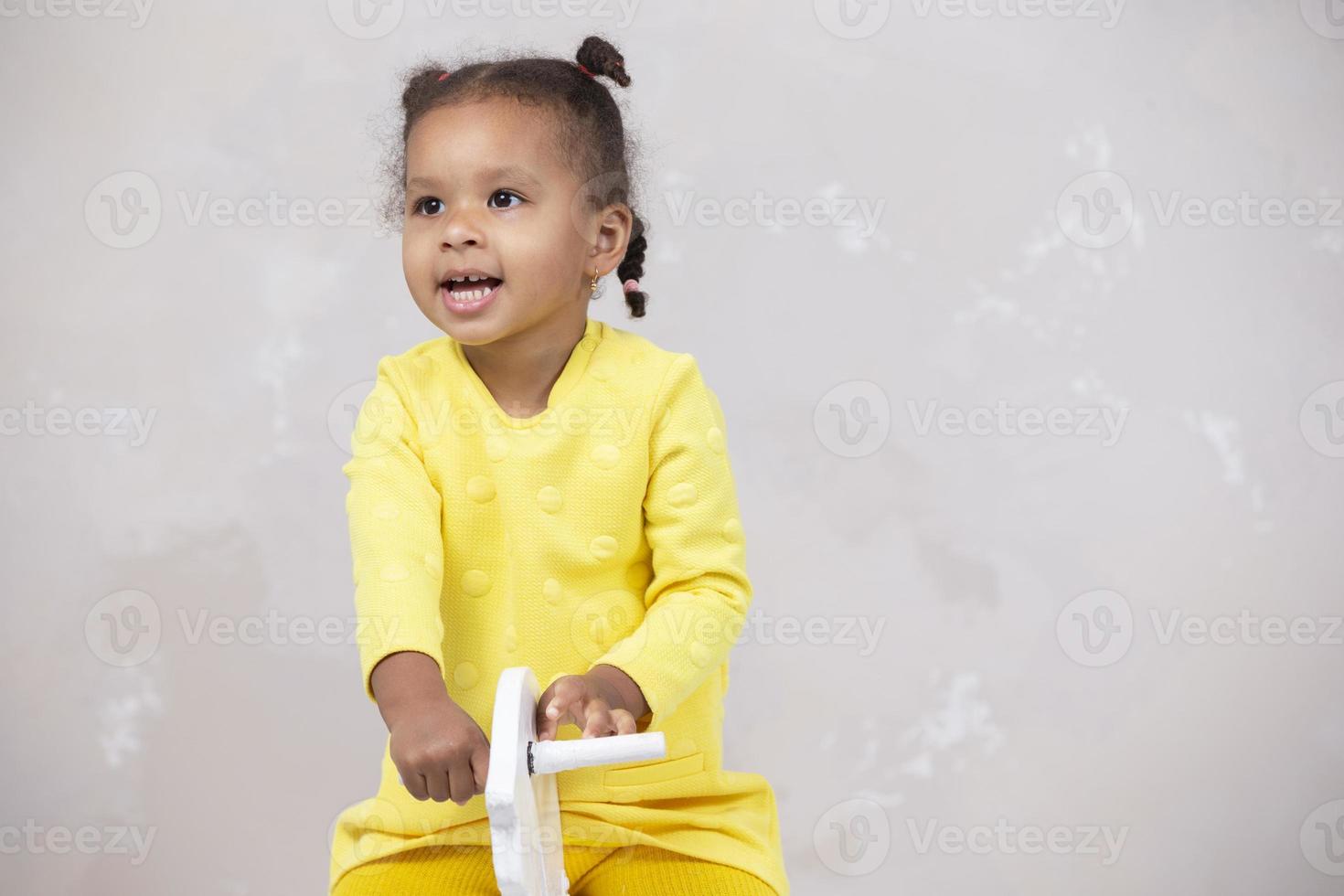 Little African American girl in yellow clothes shows tongue. Funny child. photo