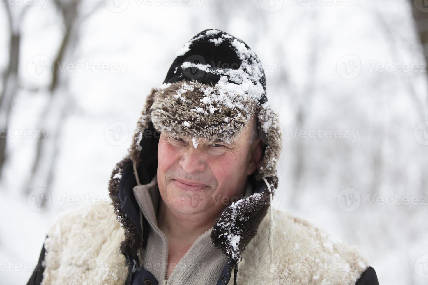 An elderly man in a winter hat covered with snow smiles and looks into the camera. photo