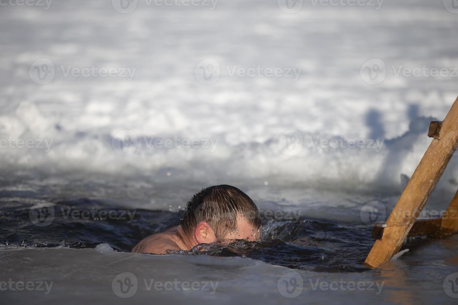 un hombre se sumerge dentro un pozo de hielo durante el invierno festival de el bautismo de Jesús. un hombre nada en el pozo de hielo en invierno. morsa gente. foto