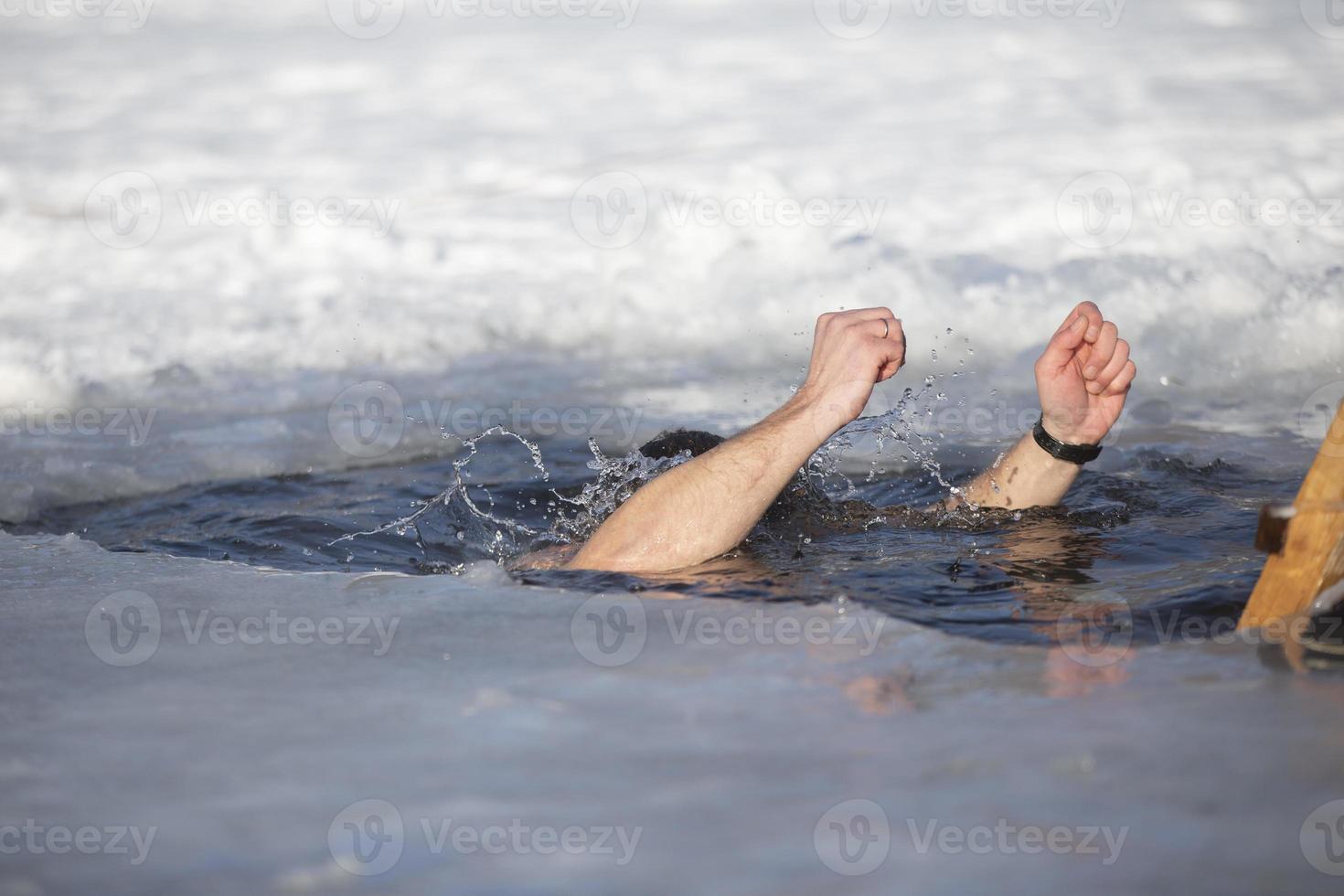 un hombre se sumerge dentro un pozo de hielo durante el invierno festival de el bautismo de Jesús. un hombre nada en el pozo de hielo en invierno. morsa gente. foto