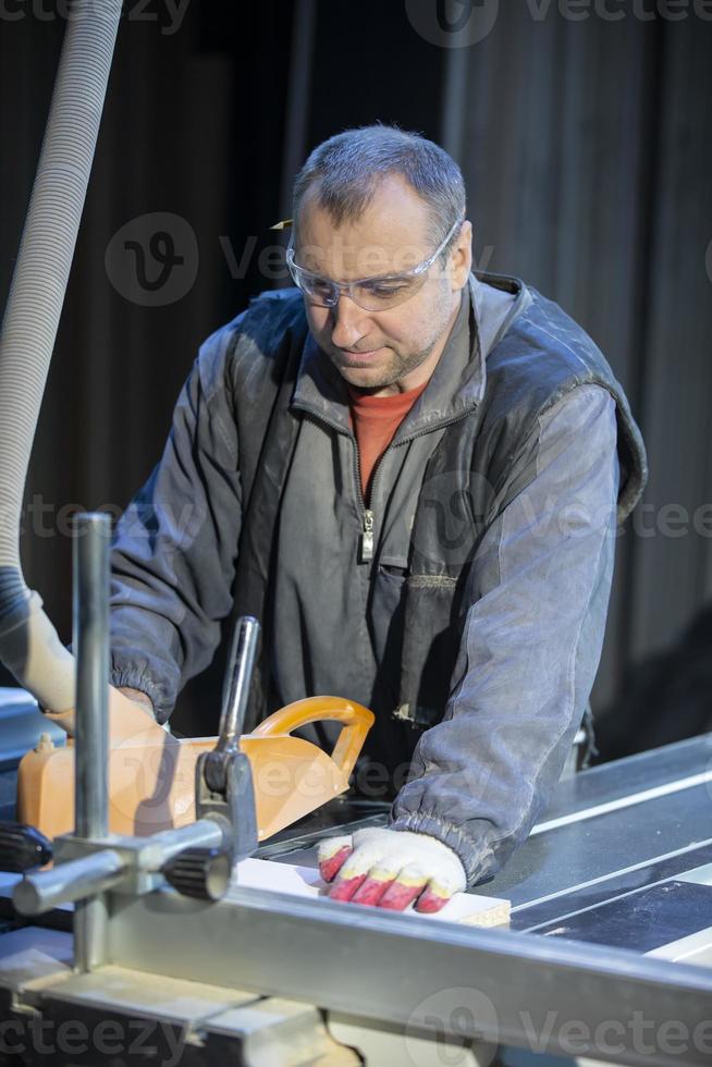 A furniture manufacturing worker at a cutting machine makes furniture parts. Furniture manufacturing. photo