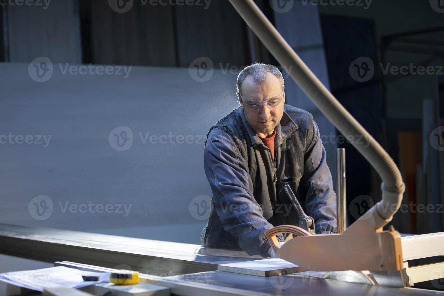 A furniture manufacturing worker at a cutting machine makes furniture parts. Furniture manufacturing. photo