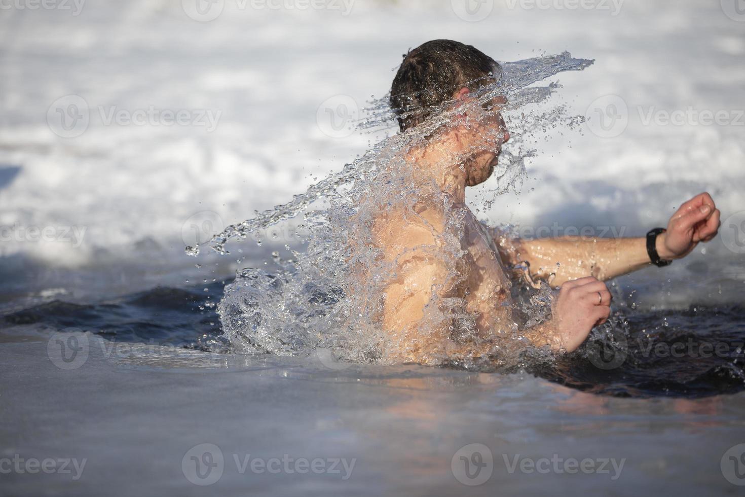 A man plunges into an ice-hole during the winter festival of the baptism of Jesus. A man swims in the ice-hole in winter. Walrus people. photo