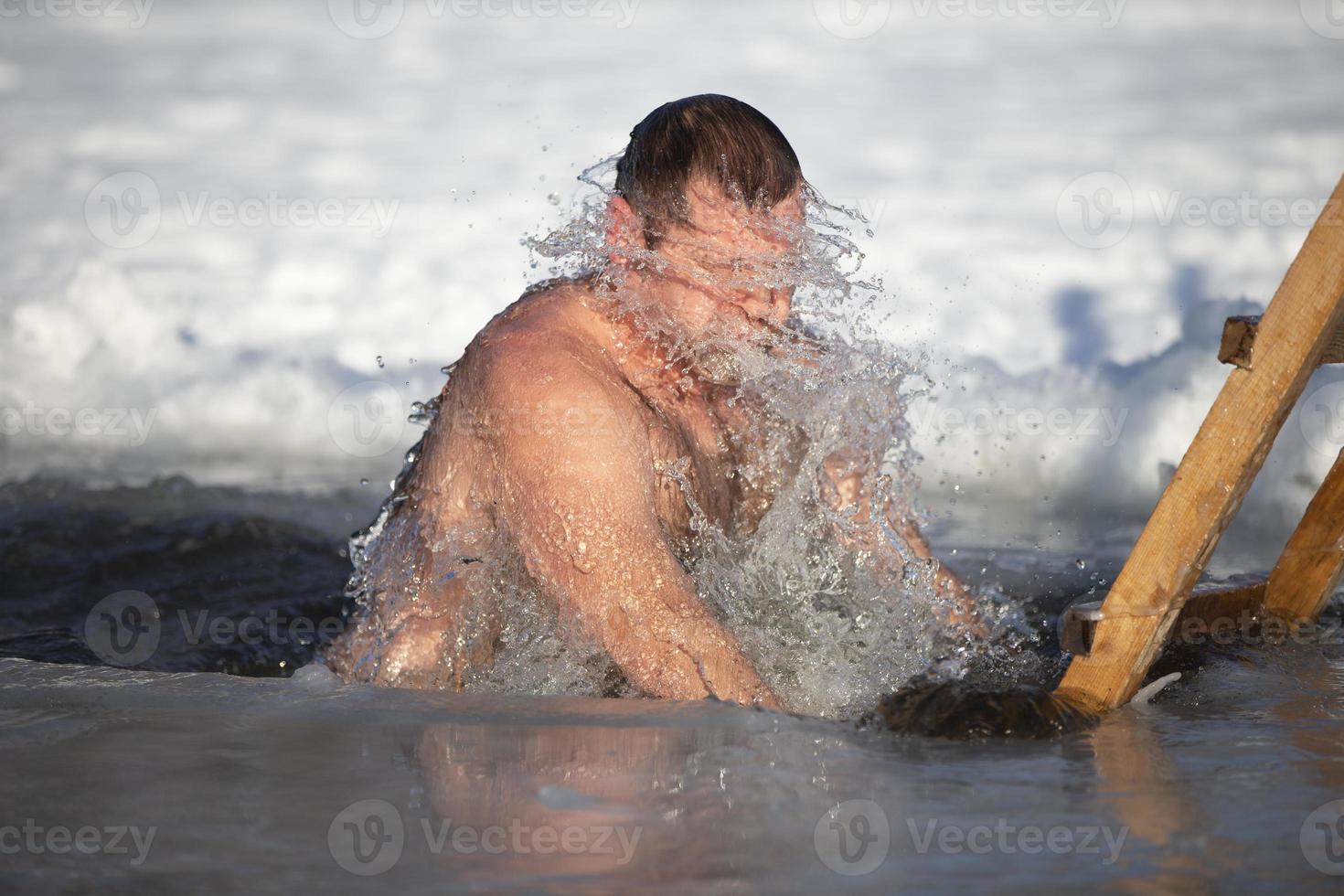 A man plunges into an ice-hole during the winter festival of the baptism of Jesus. A man swims in the ice-hole in winter. Walrus people. photo