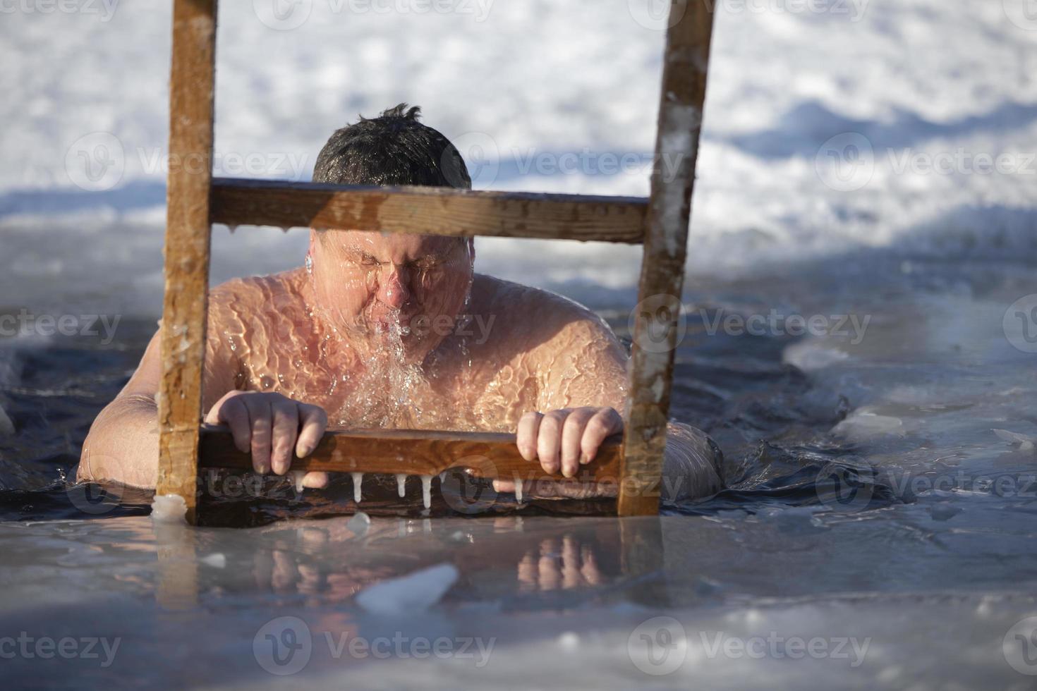 A man plunges into an ice-hole during the winter festival of the baptism of Jesus. A man swims in the ice-hole in winter. Walrus people. photo