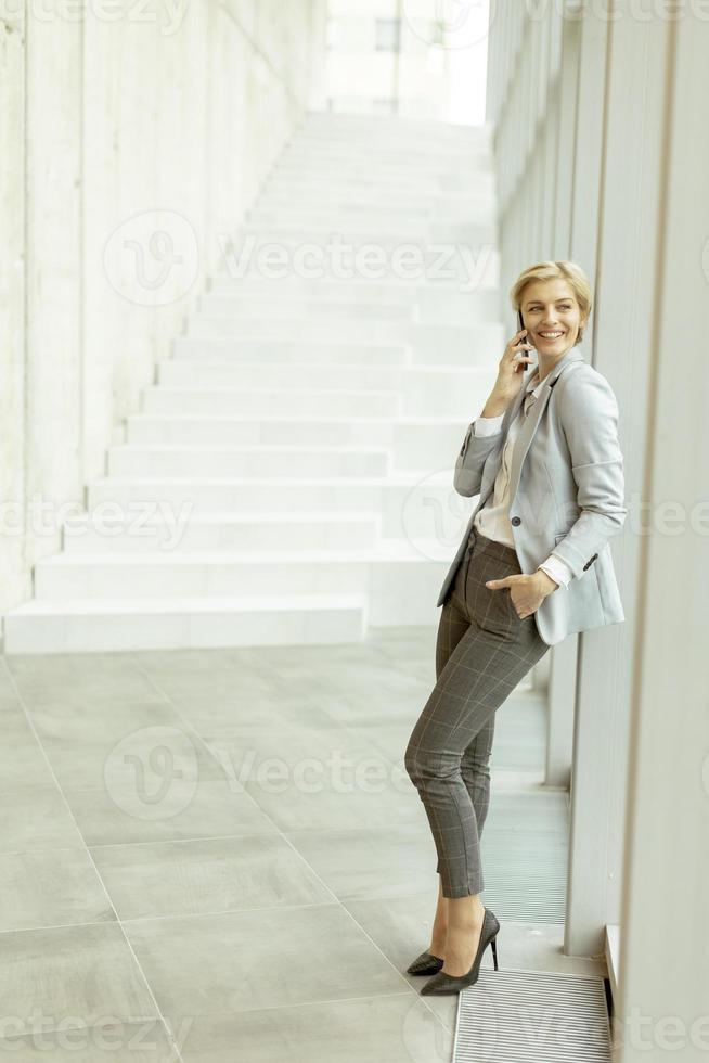 Businesswoman using mobile phone on modern office hallway photo