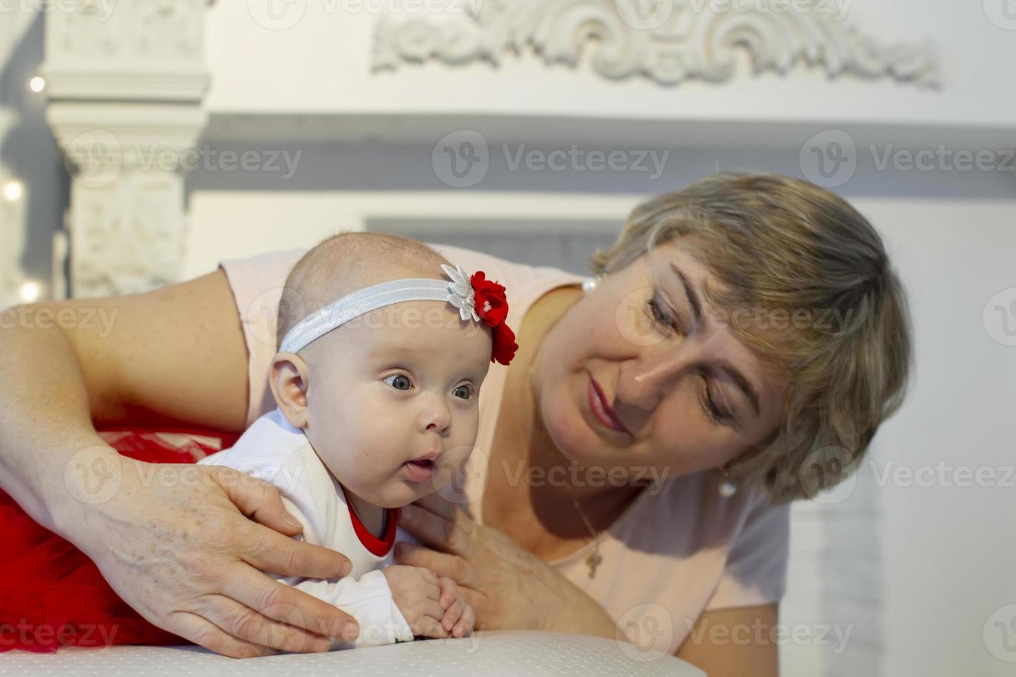 The grandmother looks at the newborn girl with love. An elderly woman and a three-month-old girl. photo