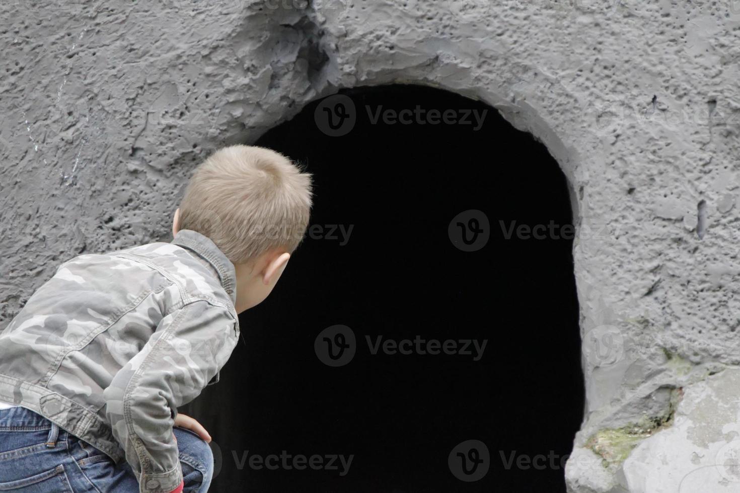 The child looks into the black hole of the cave. The concept of learning the unknown. Childish curiosity. photo