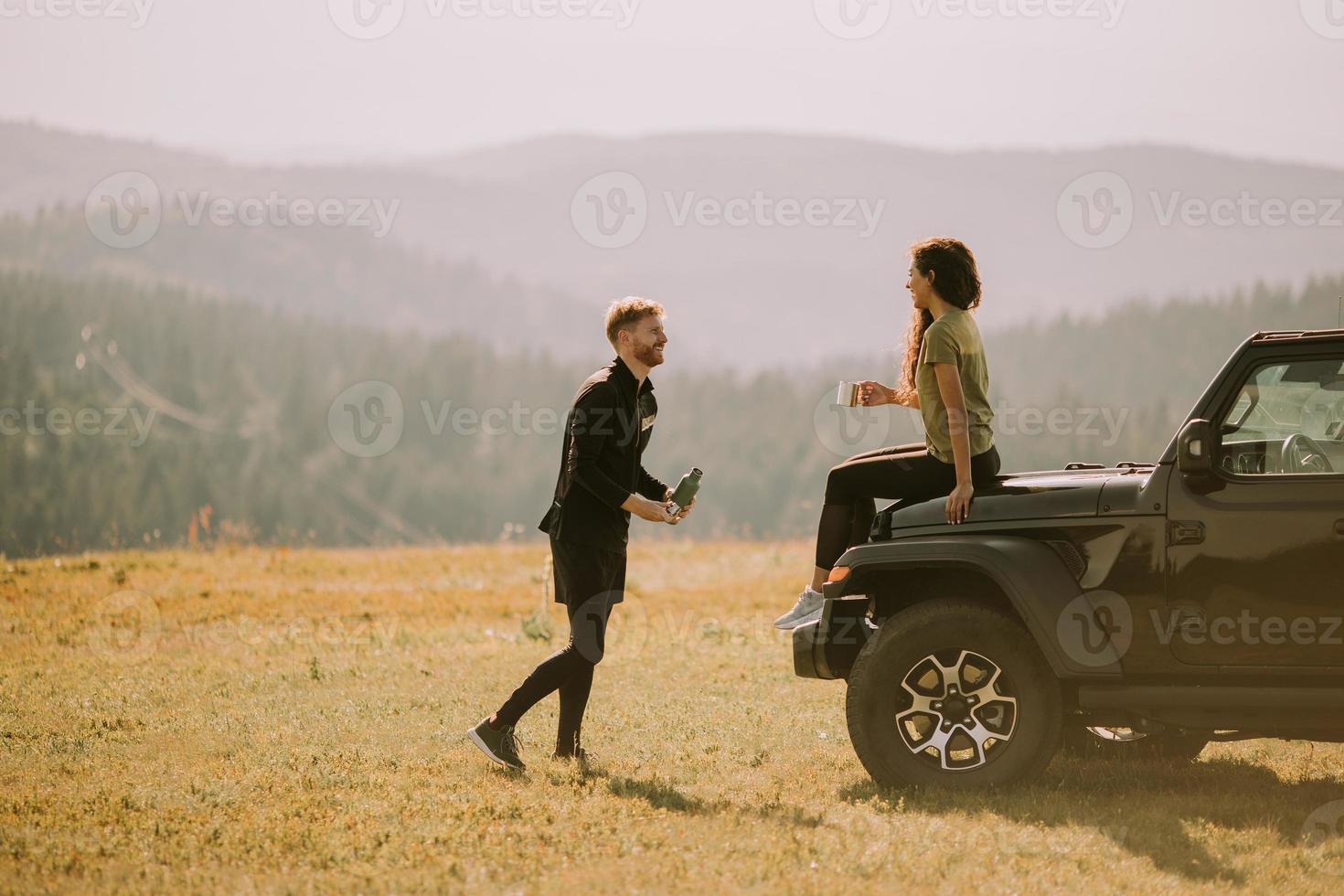 pareja joven relajándose en el capó de un vehículo de terreno en el campo foto