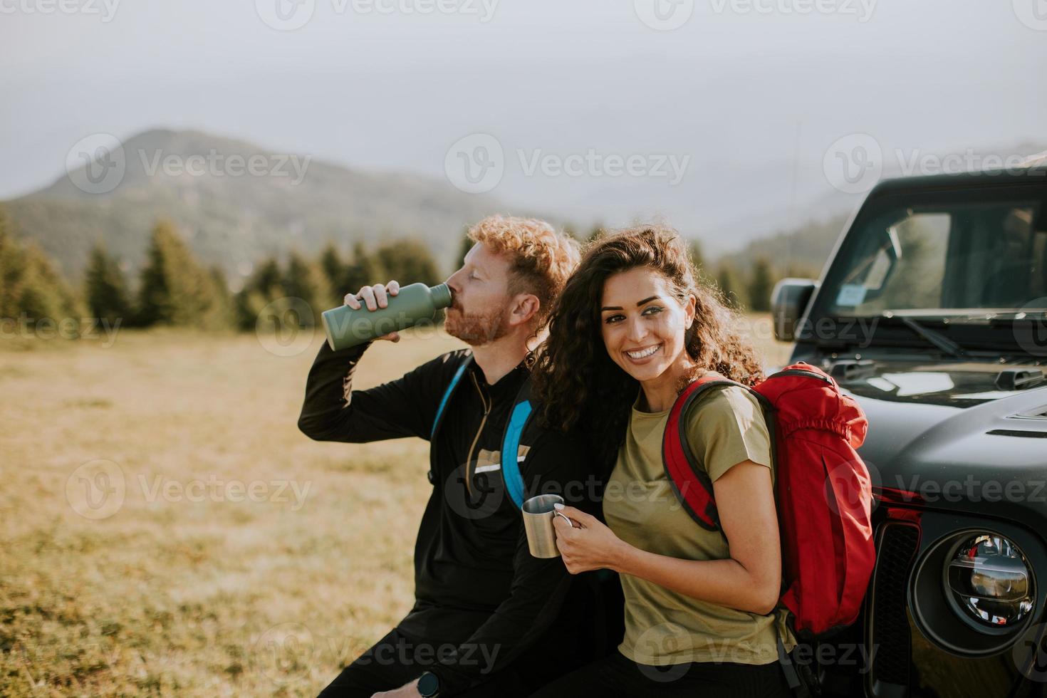 Smiling couple preparing hiking adventure with backpacks by terrain vehicle photo