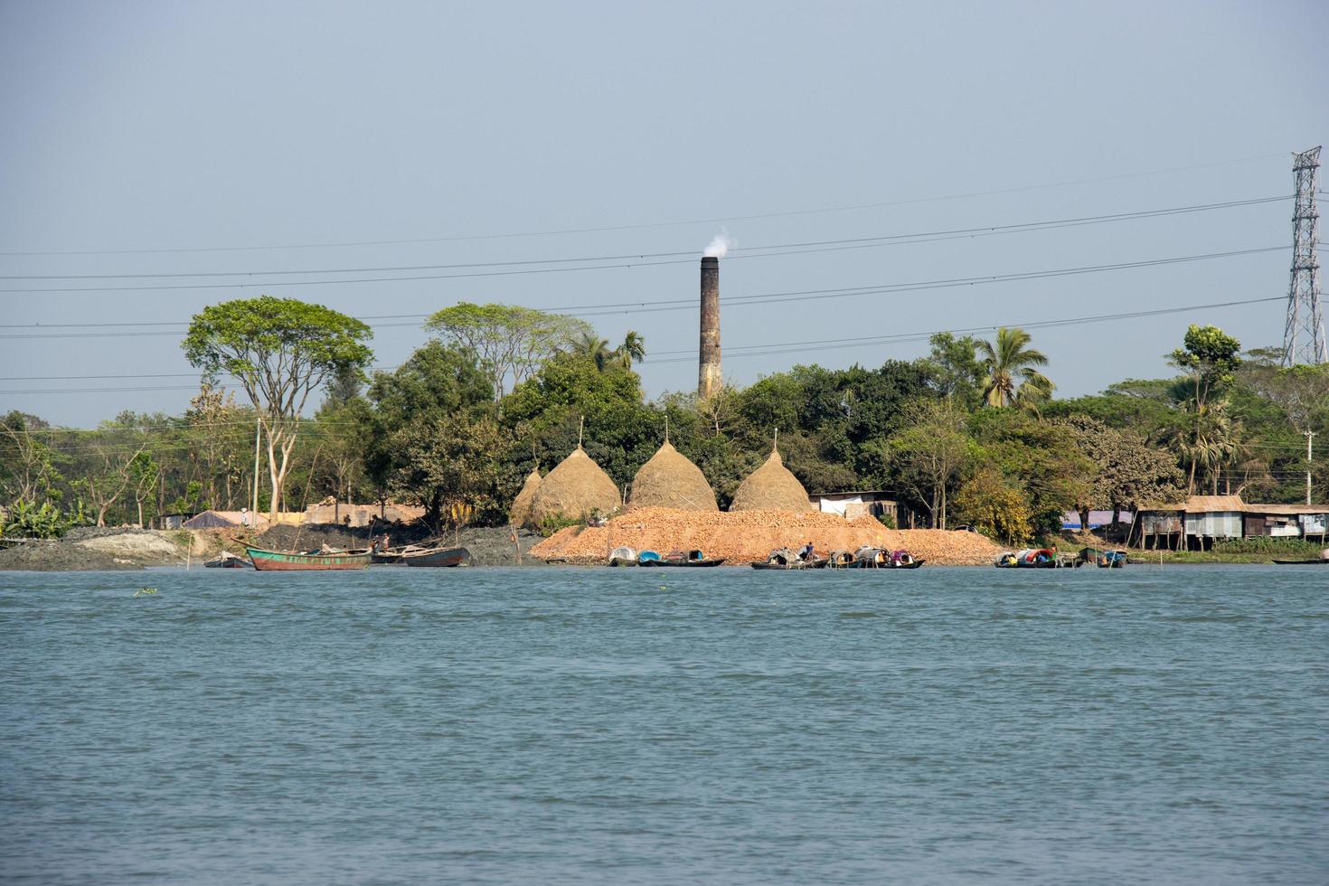 un hermosa rural zona en el banco de un río. río y pueblo zona paisaje con azul cielo. barcos en el río y enorme pajar en el orilla del río. corriente de río escénico paisaje con un ladrillo horno. foto