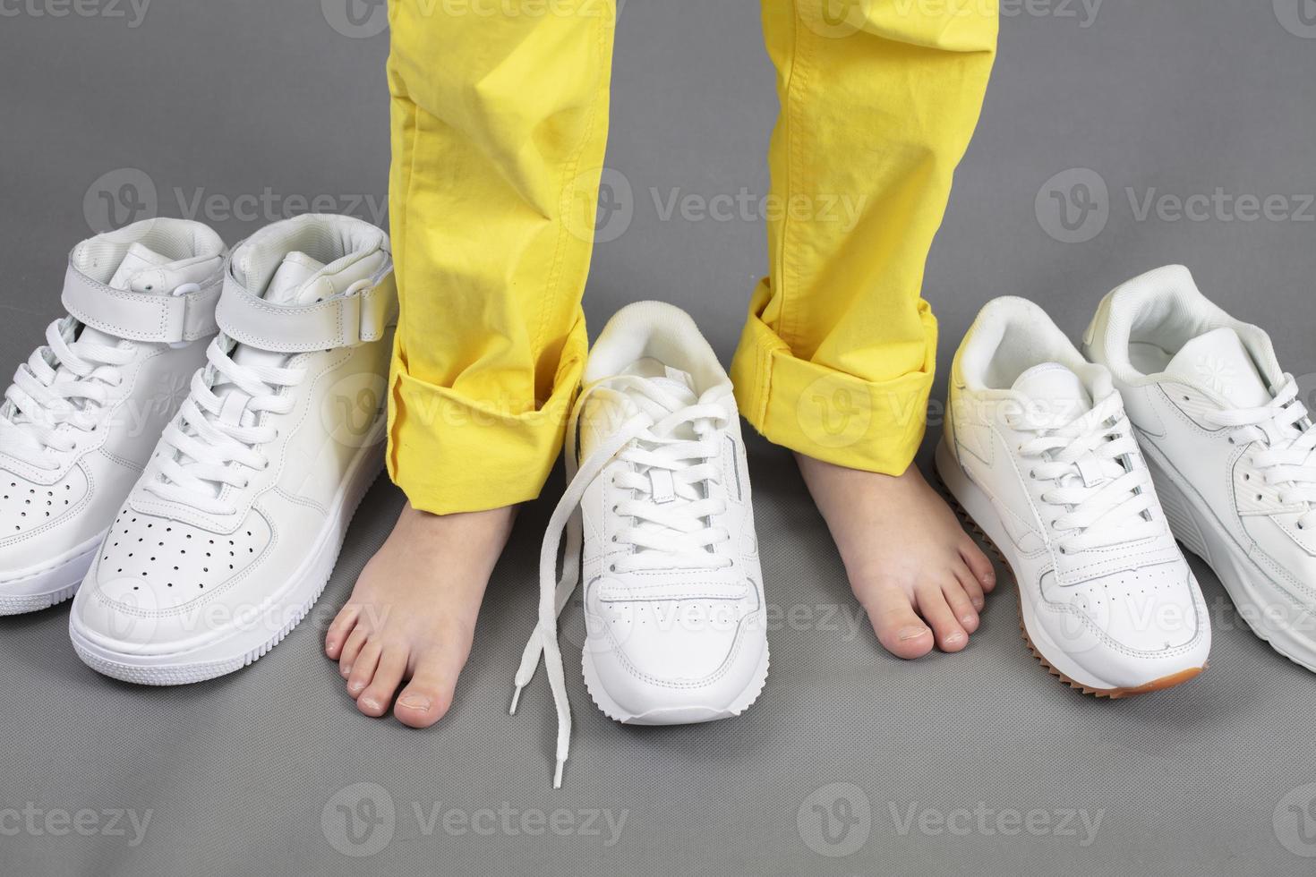 Barefoot on the background of shoes. Feet in a pile of shoes. Children's foot on the background of sneakers. Foot and shoes photo