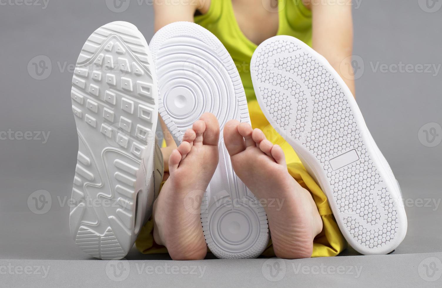 Barefoot on the background of shoes. Feet in a pile of shoes. Children's foot on the background of sneakers. Foot and shoes photo