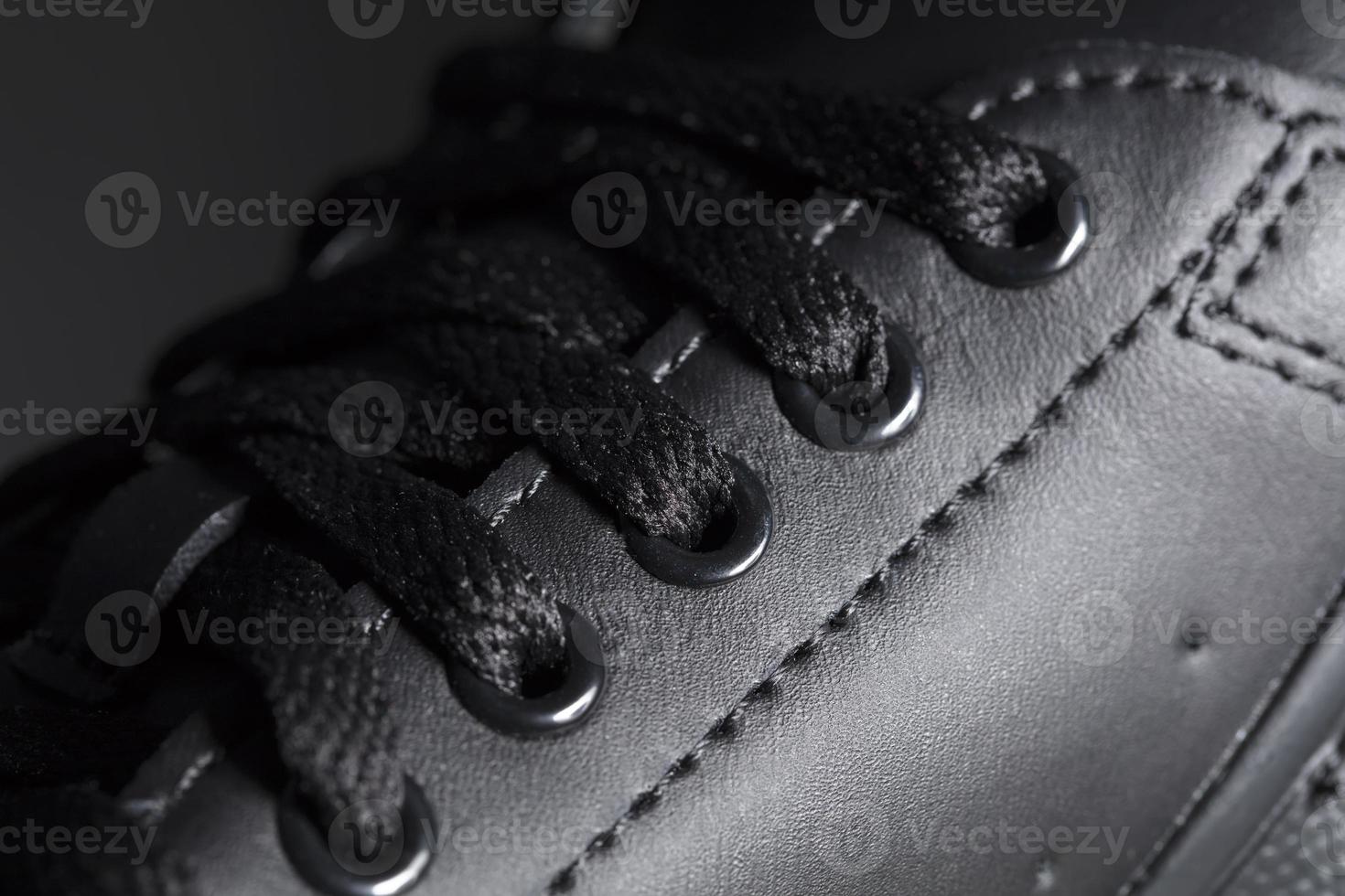 Part of a black boot with laces. A fragment of dark shoes. A piece of sneaker. photo