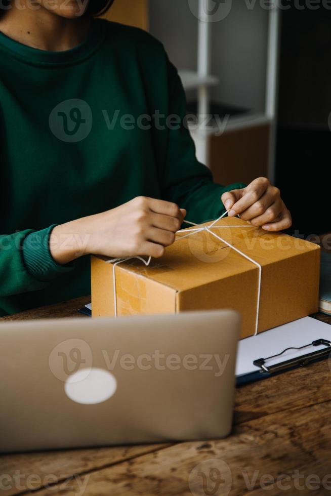 Startup small business entrepreneur or freelance Asian woman using a laptop with box, Young success Asian woman with her hand lift up, online marketing packaging box and delivery, SME concept. photo