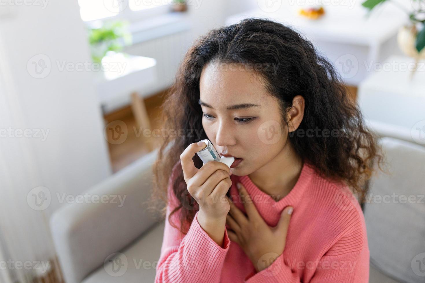 asiático mujer utilizando inhalador mientras sufrimiento desde asma a hogar. joven mujer utilizando asma inhalador. de cerca de un joven asiático mujer utilizando asma inhalador a hogar. foto