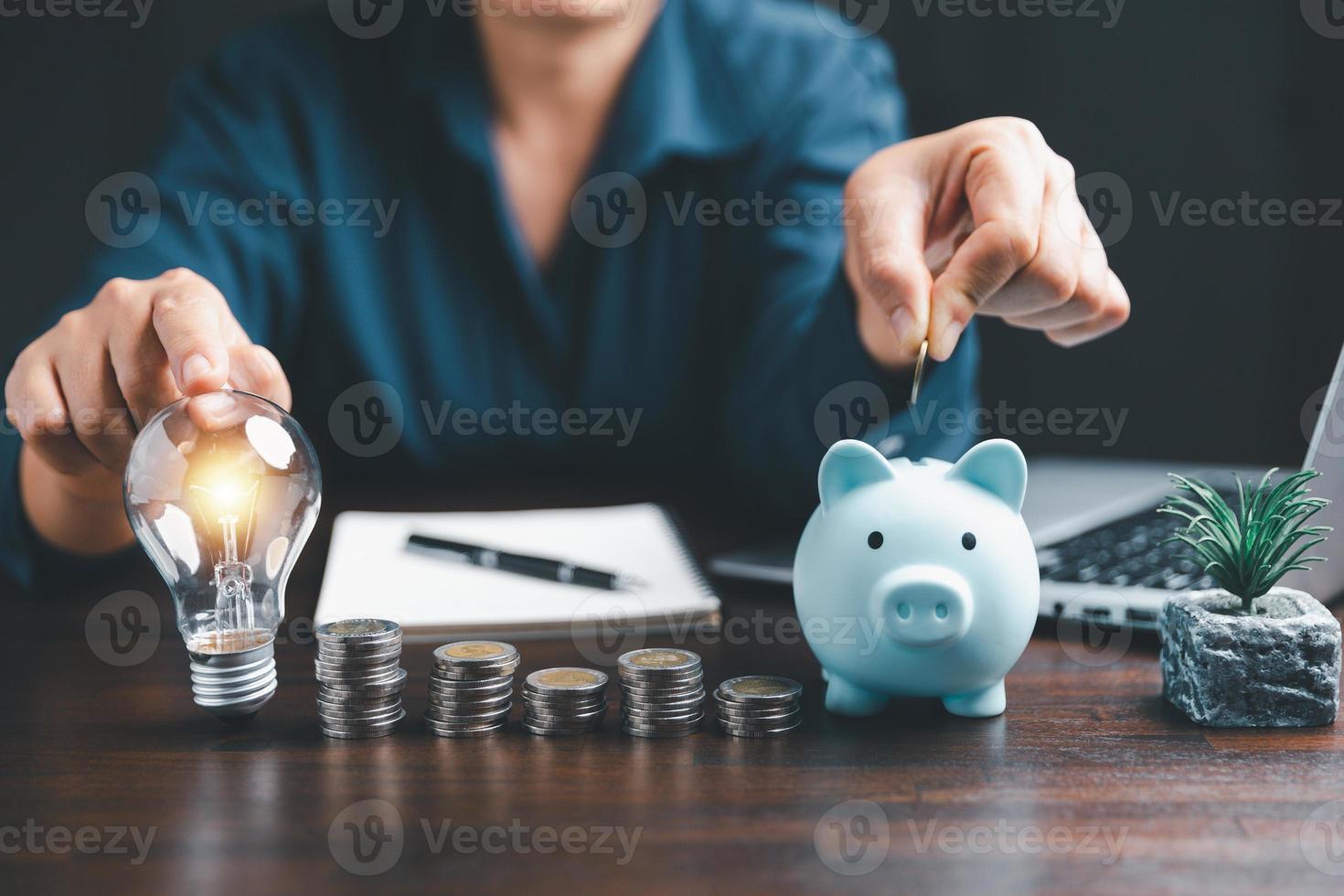 Businesswoman with lightbulb and piggy bank and using calculator to calculate and money stack. Save energy and money with accounting finance in office concept. Idea of energy saving planning in home. photo