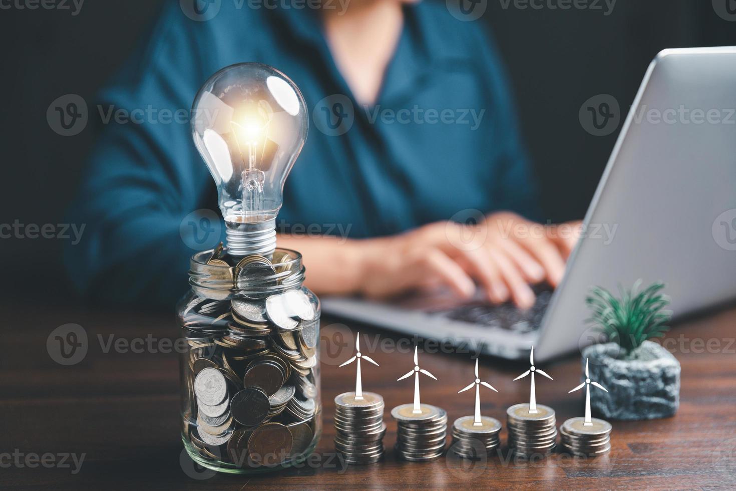 Businesswoman with lightbulb on money jar and using calculator to calculate and money stack. Save energy and money with accounting finance in office concept. Idea of energy saving planning in home. photo