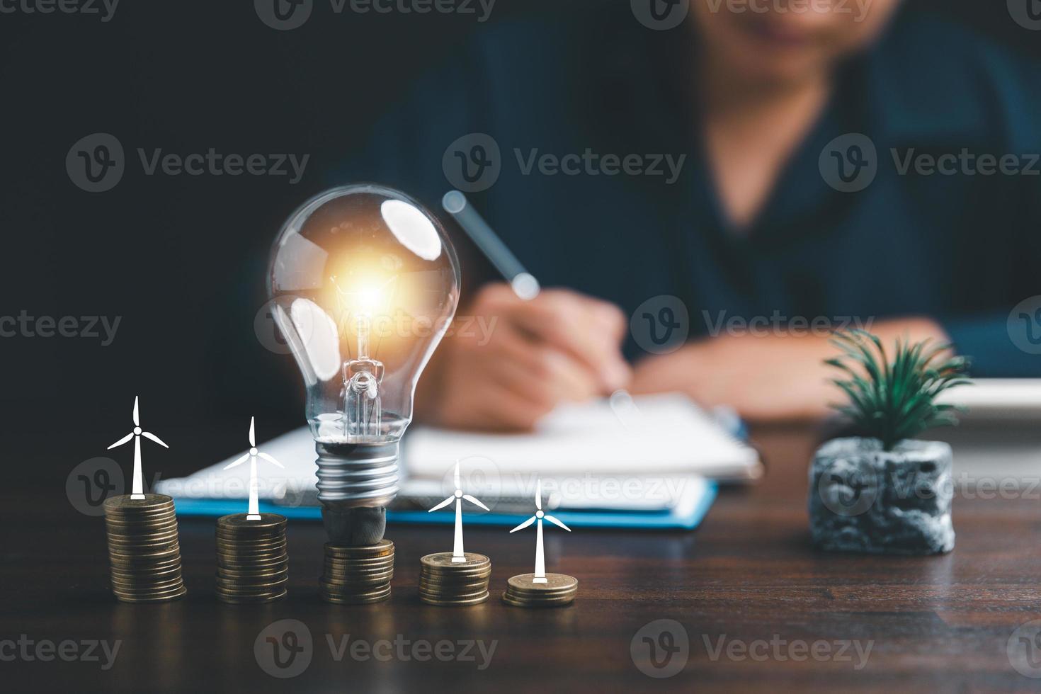 Businesswoman with lightbulb on coins and using calculator to calculate and money stack. Save energy and money with accounting finance in office concept. Idea of energy saving planning in home. photo