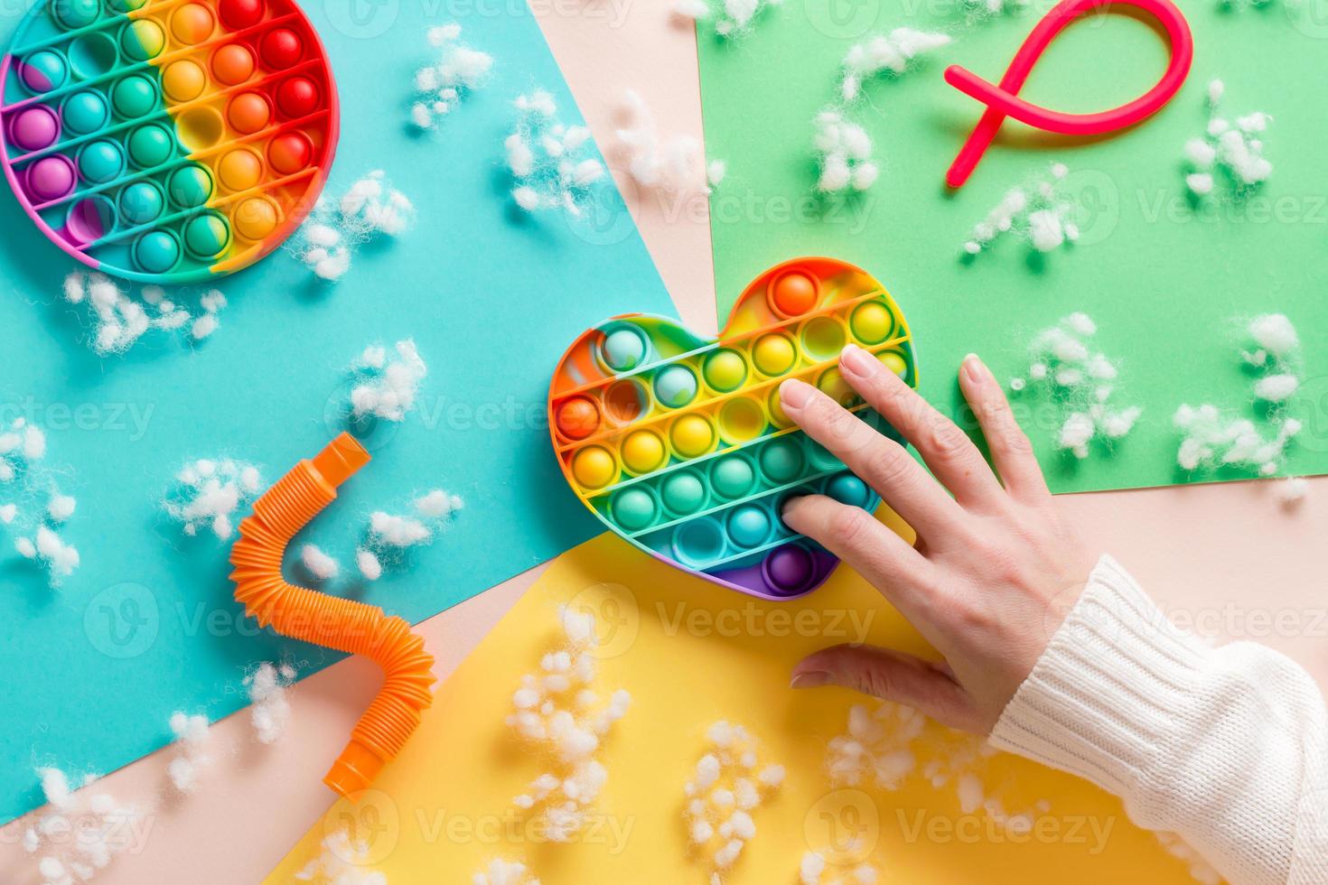 De las mujeres manos prensa en un silicona arco iris anti estrés juguete en el forma de un corazón y otro juguetes en un cartulina de diferente colores y pelusa. relajación y tranquilidad foto