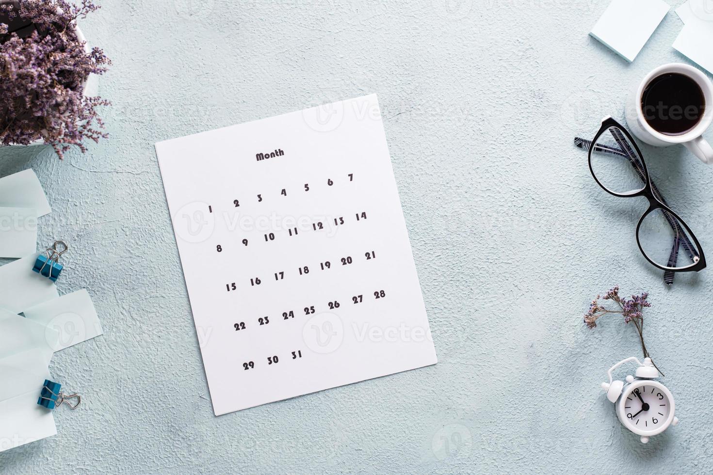 blanco sábana de mensual calendario, anteojos, café taza y alarma reloj en el escritorio. hora planificación y organización foto