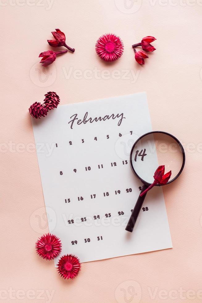 San Valentín día. un aumentador vaso Destacar el fecha febrero 14 en un calendario sábana y seco flores en un rosado antecedentes. parte superior y vertical ver foto