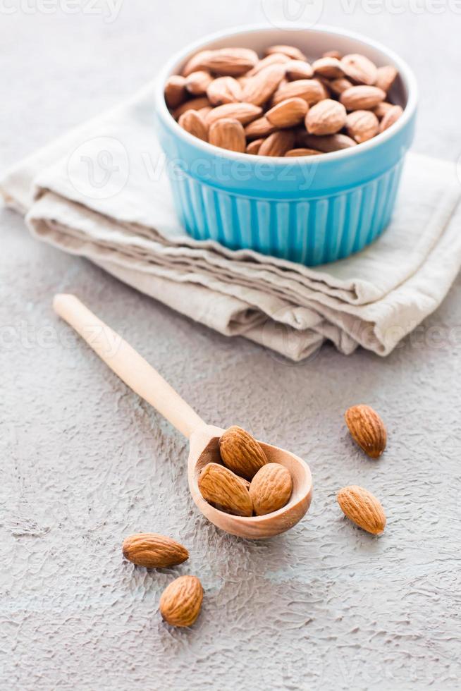 Fresh peeled almonds in a wooden spoon and in a bowl nearby on a light background. A source of vitamins and oils. Organic food. Vertical view photo