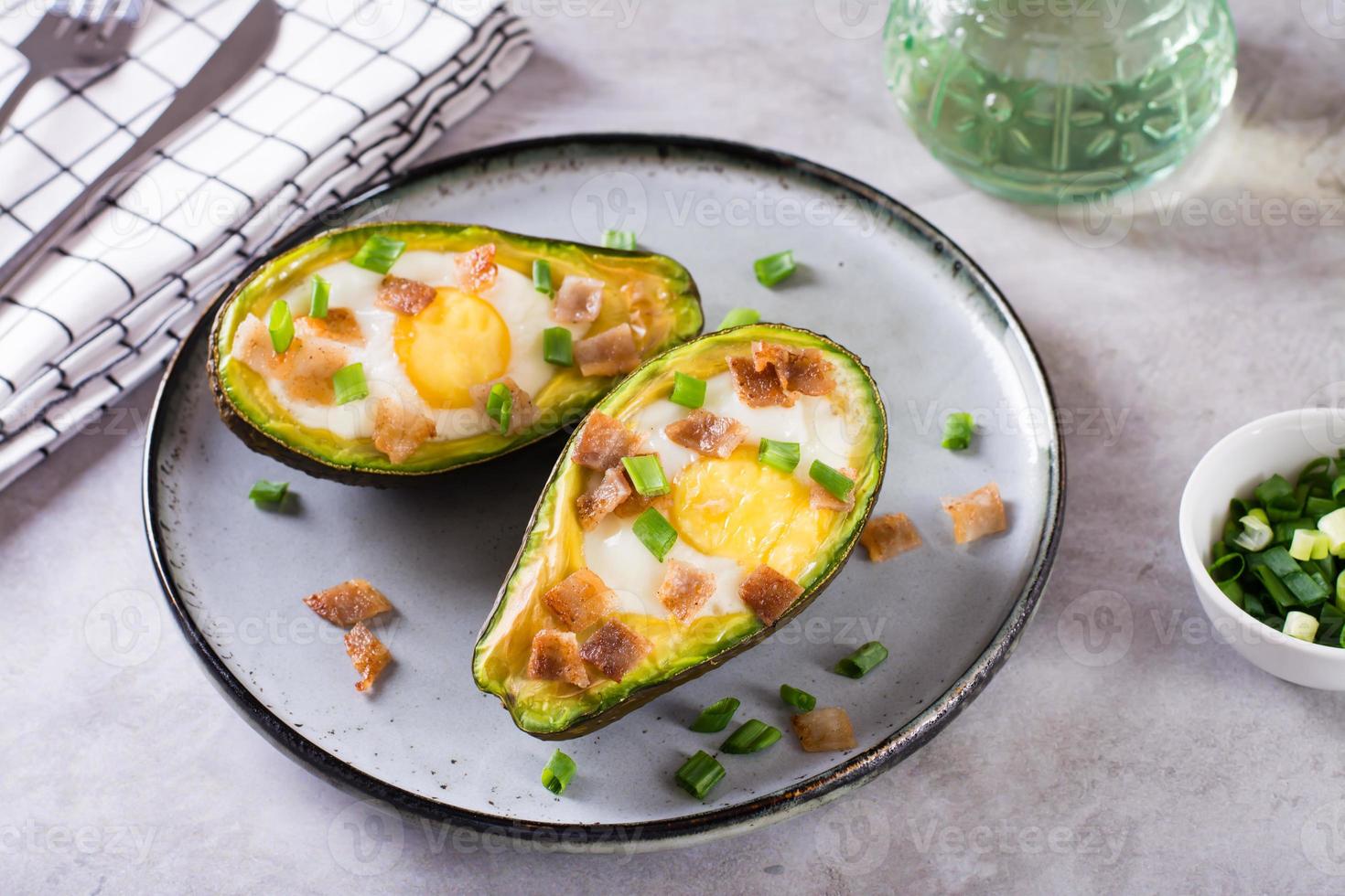 huevo horneado en aguacate rociado con tocino y hierbas en un plato foto