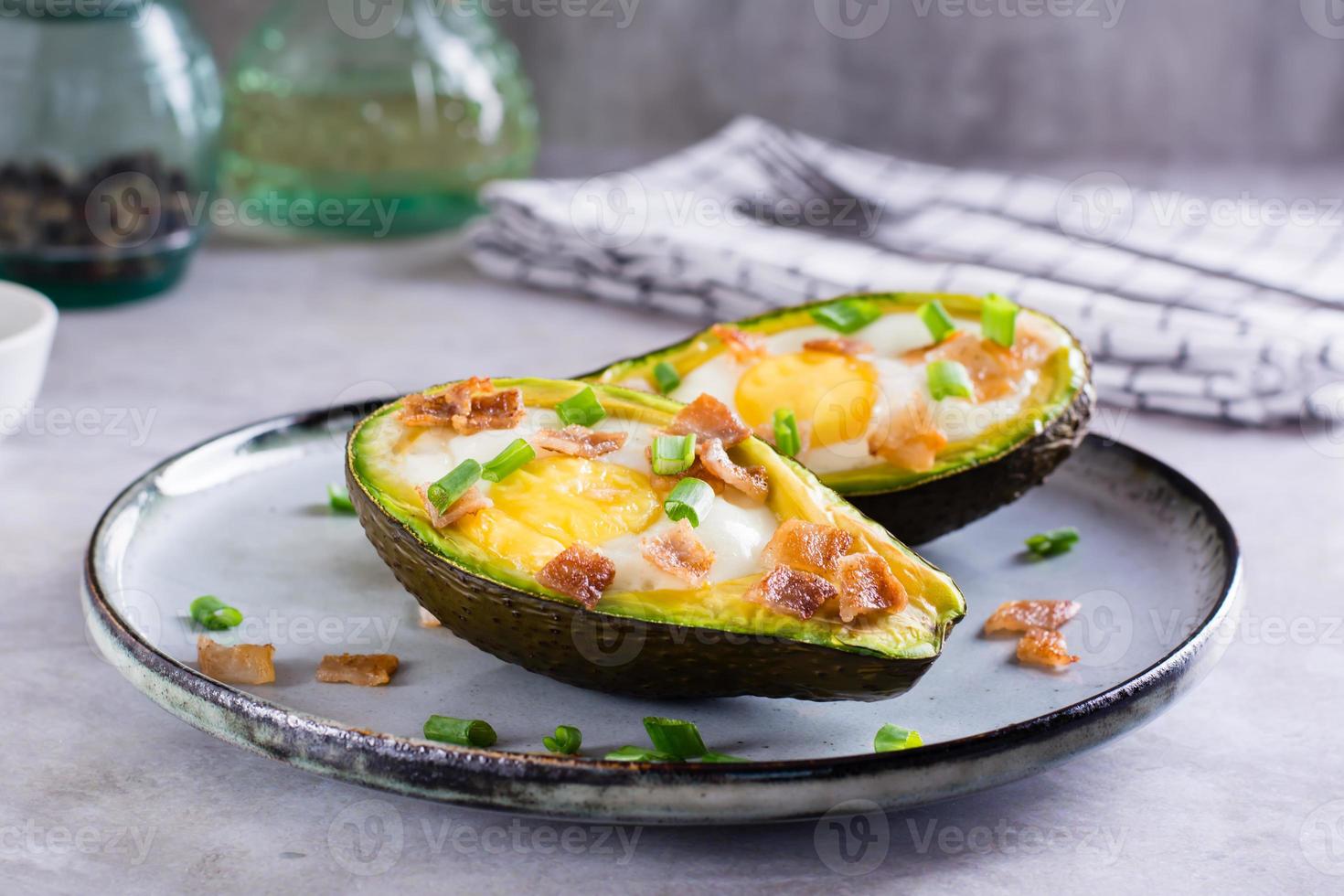 Baked avocado with egg, bacon and chives on a plate on the table for a keto diet photo