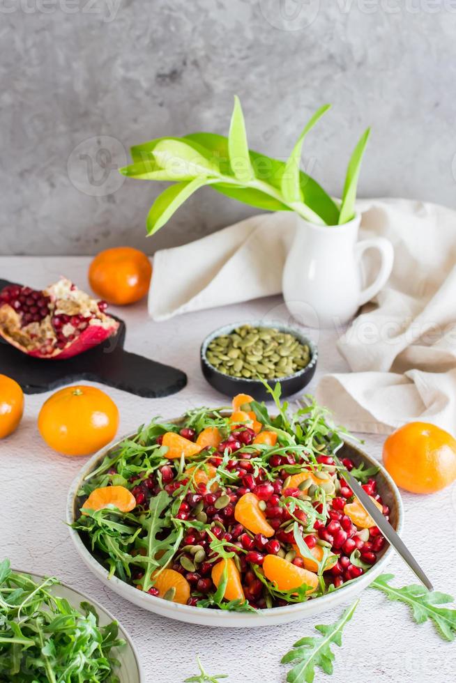 Ready to eat fruit salad of pomegranate, tangerine, arugula and pumpkin seeds in a plate on the table. Organic vegetarian food. photo