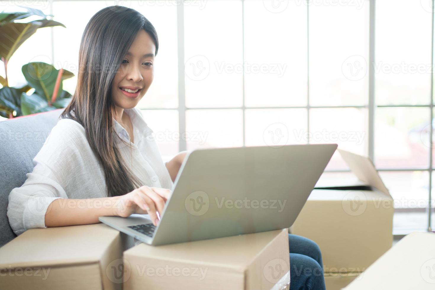 Happy young Asian woman entrepreneur, Smile for sales success after checking order from online shopping store in laptop at home office, Concept of merchant business online and eCommerce photo