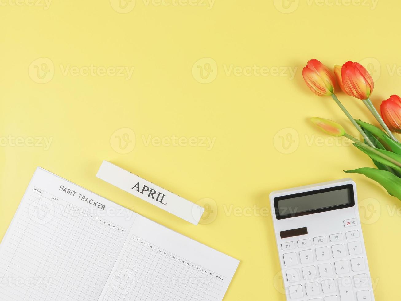 flat layout of Habit tracker book,  white calculator, wooden calendar April and tulips on yellow background. photo